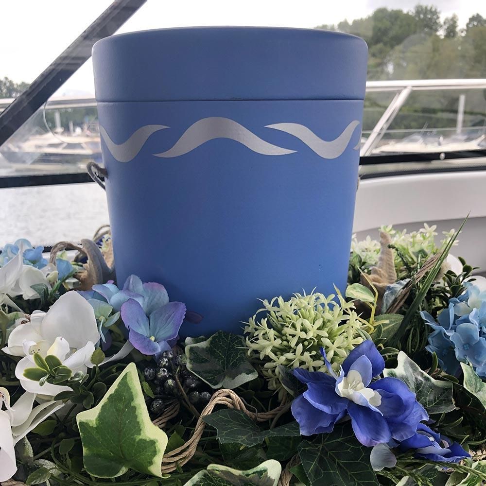 Eine blaue Urne ist von Blumen und Blättern umgeben auf einem Tisch.