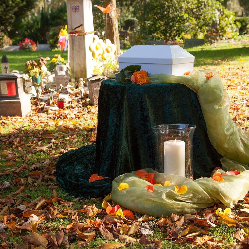 Ein Tisch mit einer Kerze und Blumen darauf auf einem Friedhof