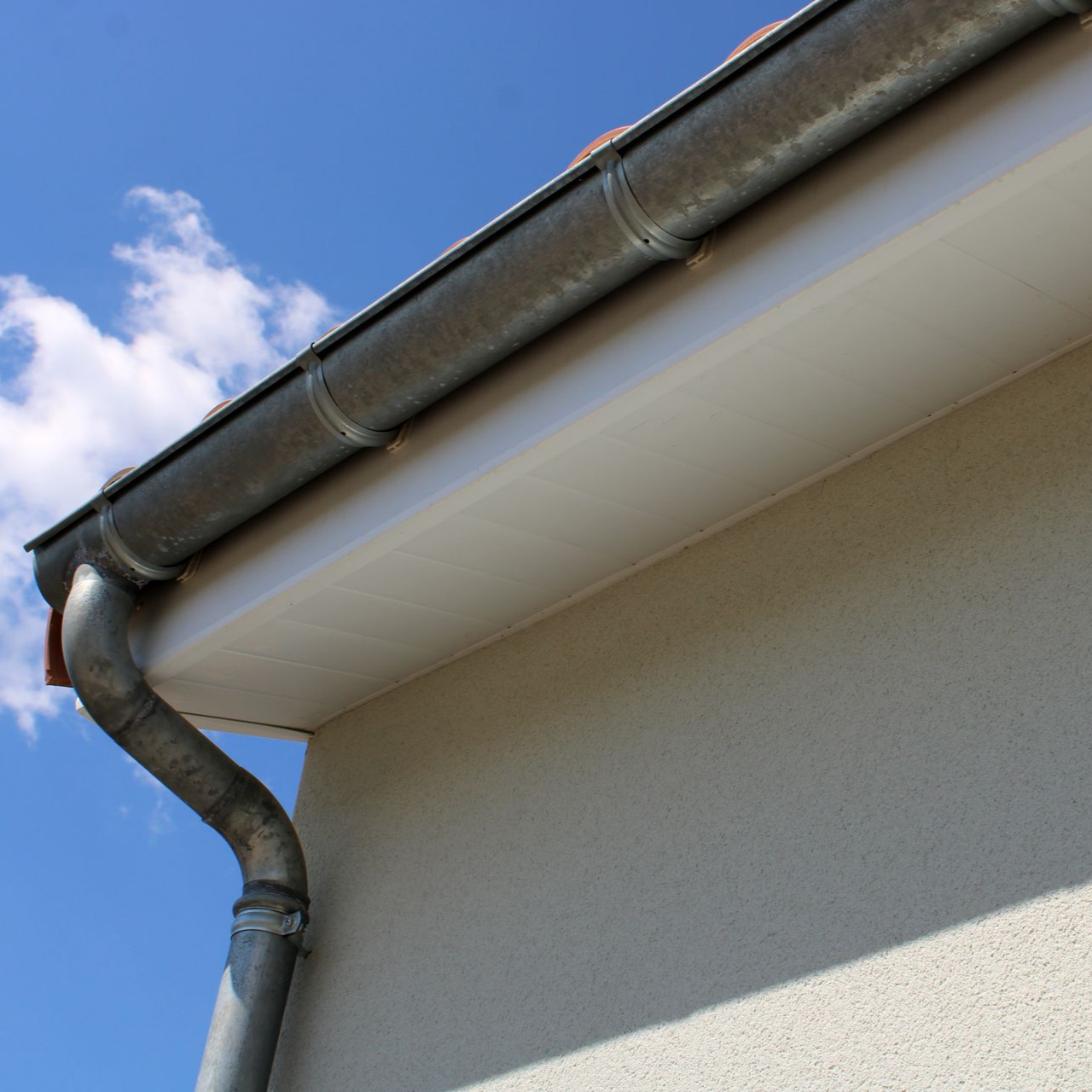 Gouttière et descente pluviale sur une maison, sur fond de ciel bleu nuageux.
