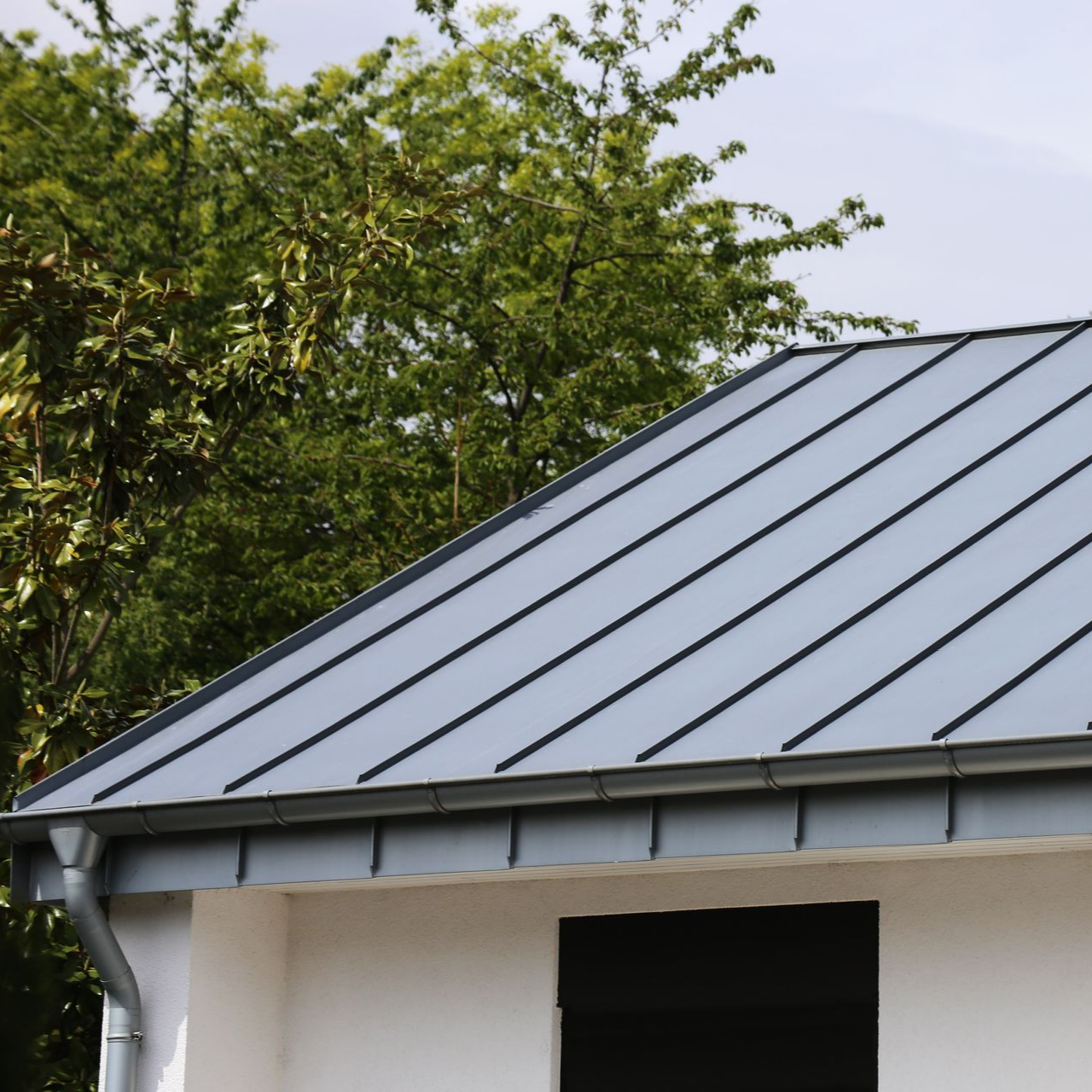 Toit en métal gris sur une maison blanche avec des arbres en arrière-plan.