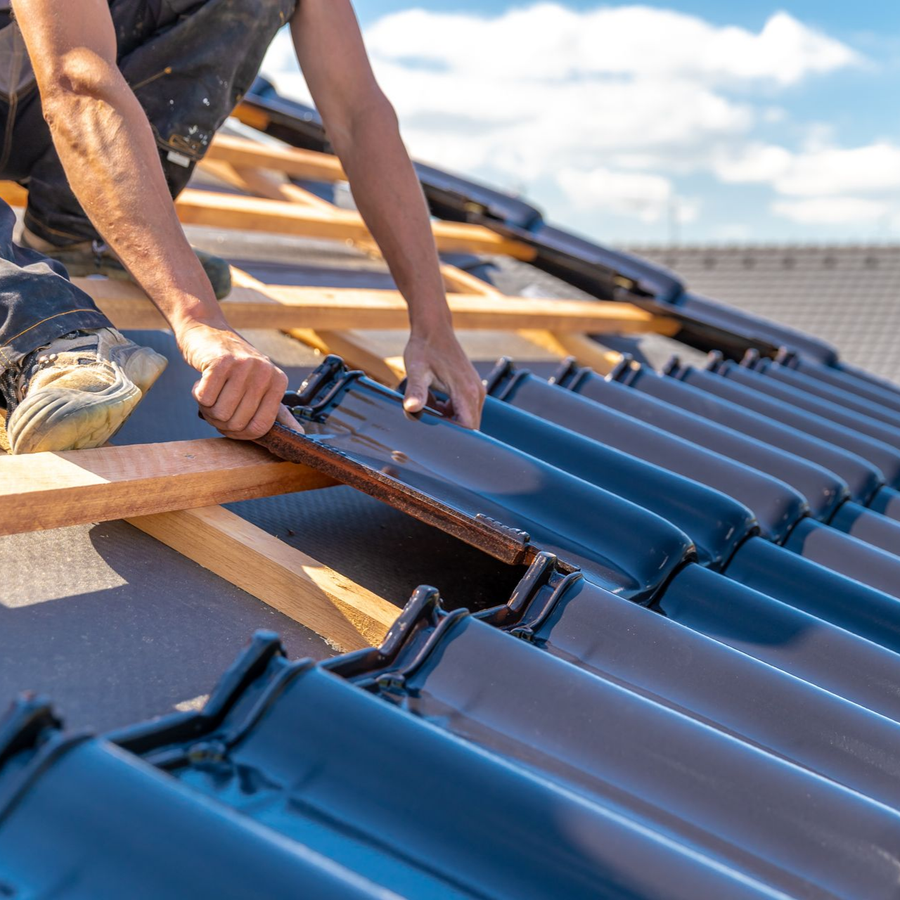 Un couvreur pose des tuiles sur une charpente en bois.