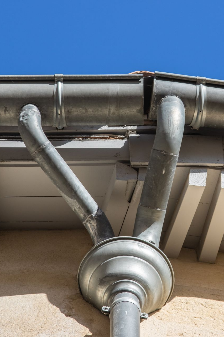 Système de gouttières métalliques avec trois descentes pluviales.