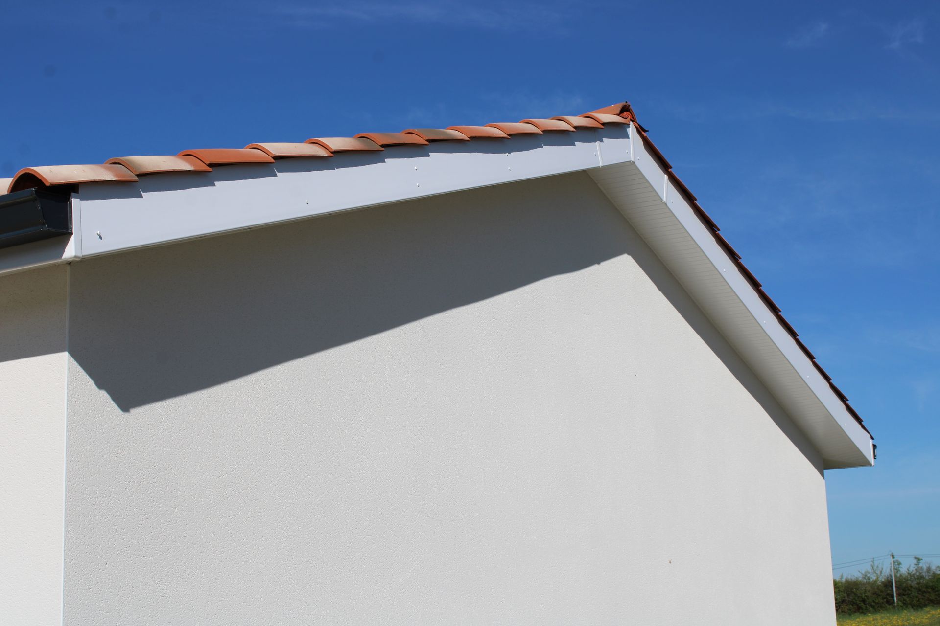 Façade blanche d'un bâtiment avec un toit de tuiles en terre cuite et un habillage de planches de rive