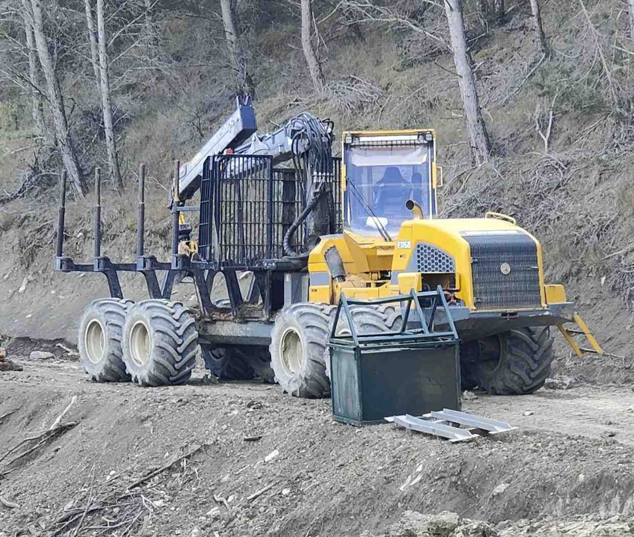 Maquina maderera amarilla en un camino de tierra en un bosque.