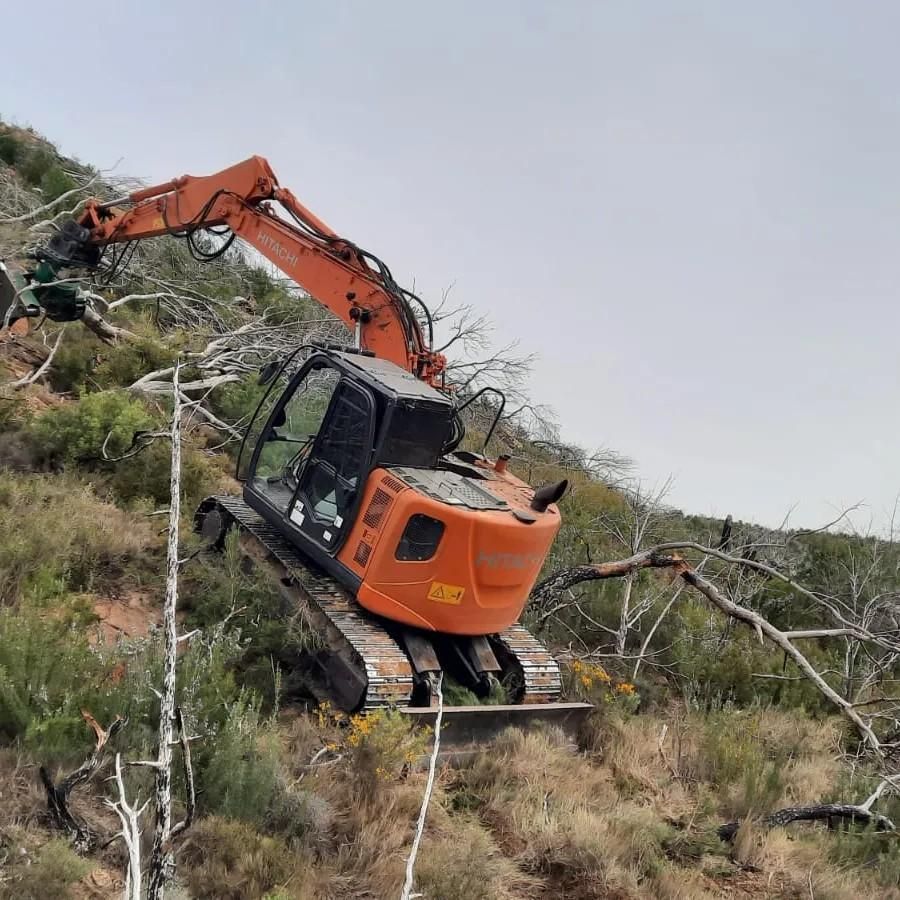 Excavadora naranja en una ladera limpiando maleza muerta.