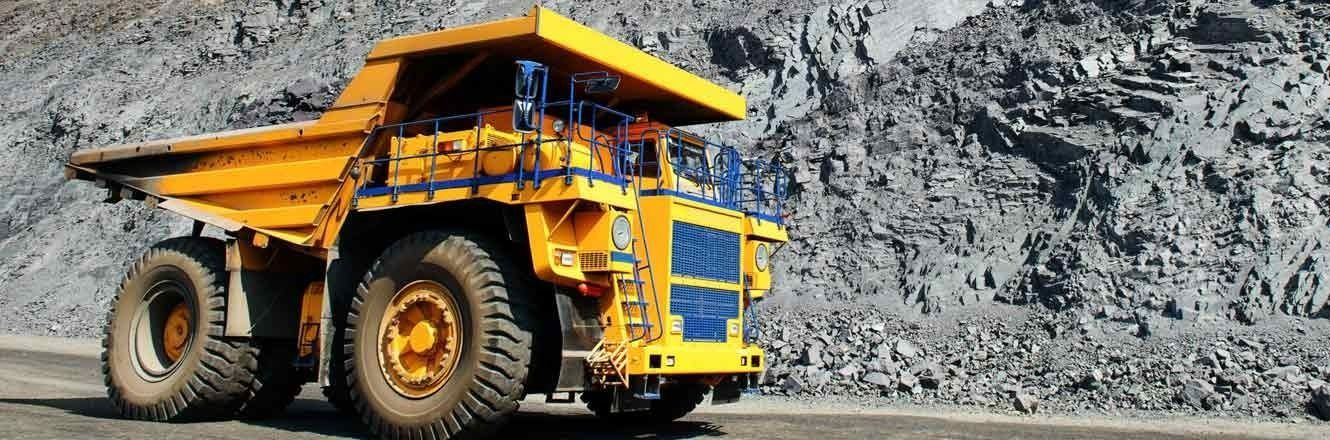 Un gran camión volquete amarillo circula por un camino de tierra.