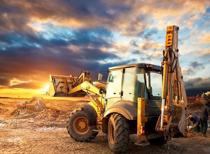 Una excavadora está trabajando en un sitio de construcción al atardecer.