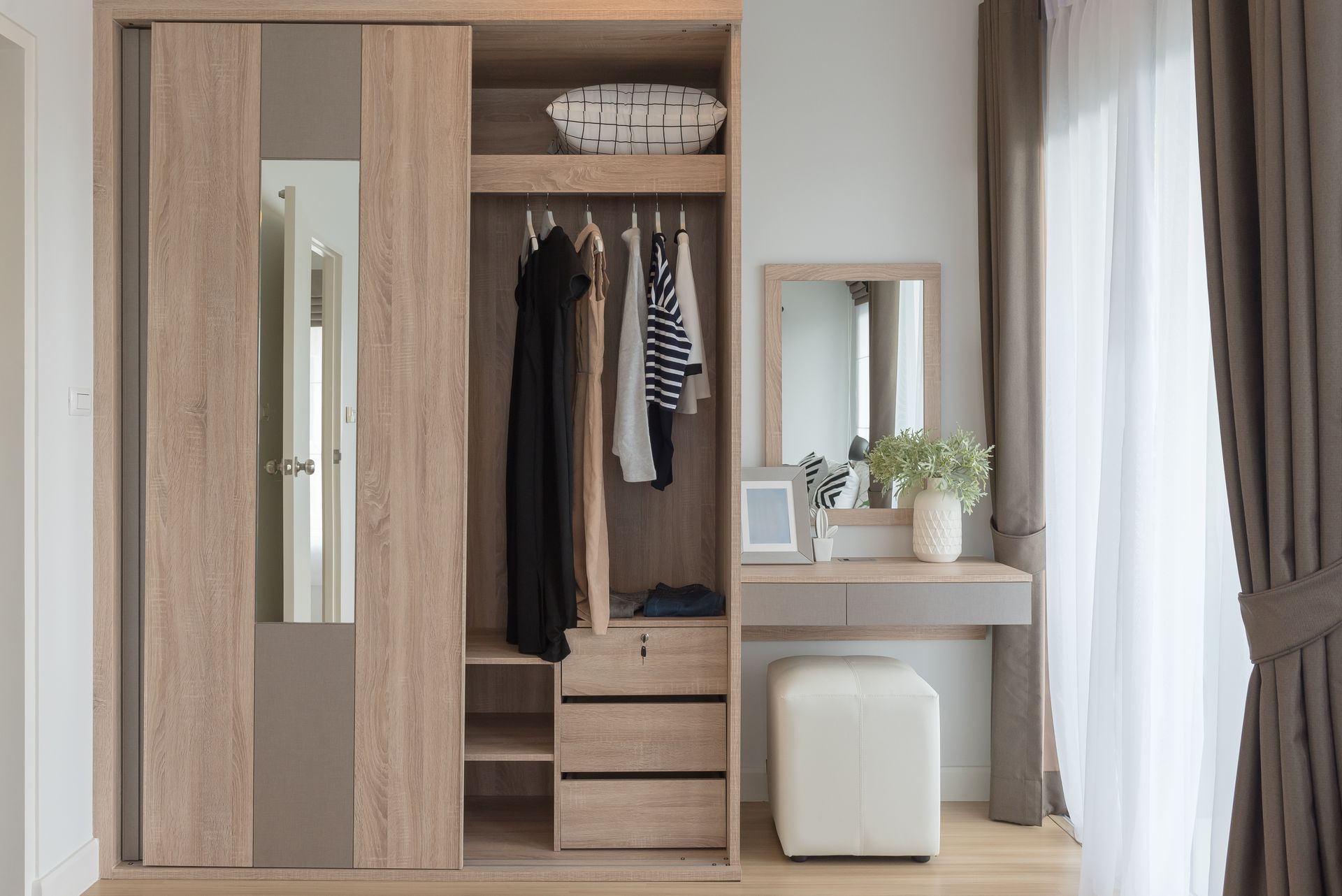Armoire en bois avec vêtements, miroir, coiffeuse et rideaux.
