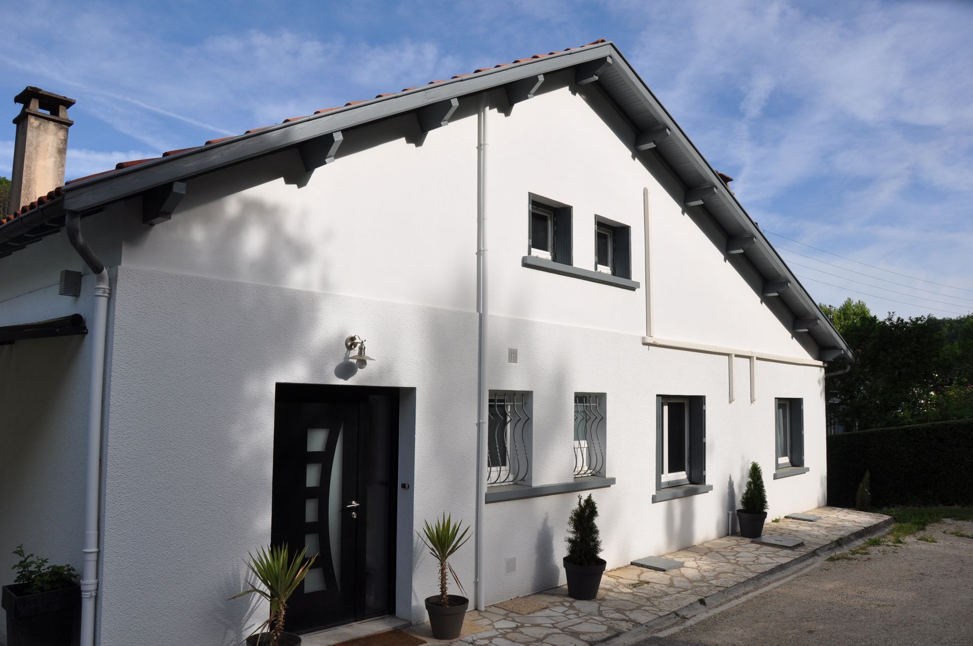 Maison en construction avec échafaudages ; murs blancs, tuyau rouge, ciel bleu.