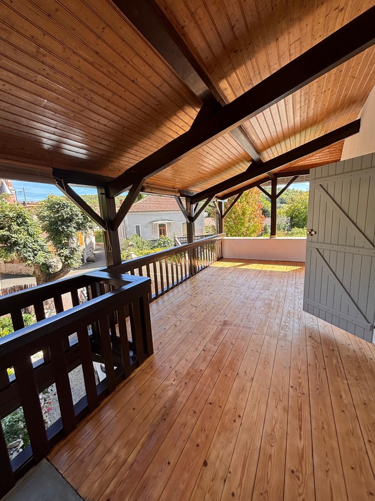 Porche en bois avec une rampe marron, une porte ouverte et des chevrons apparents.