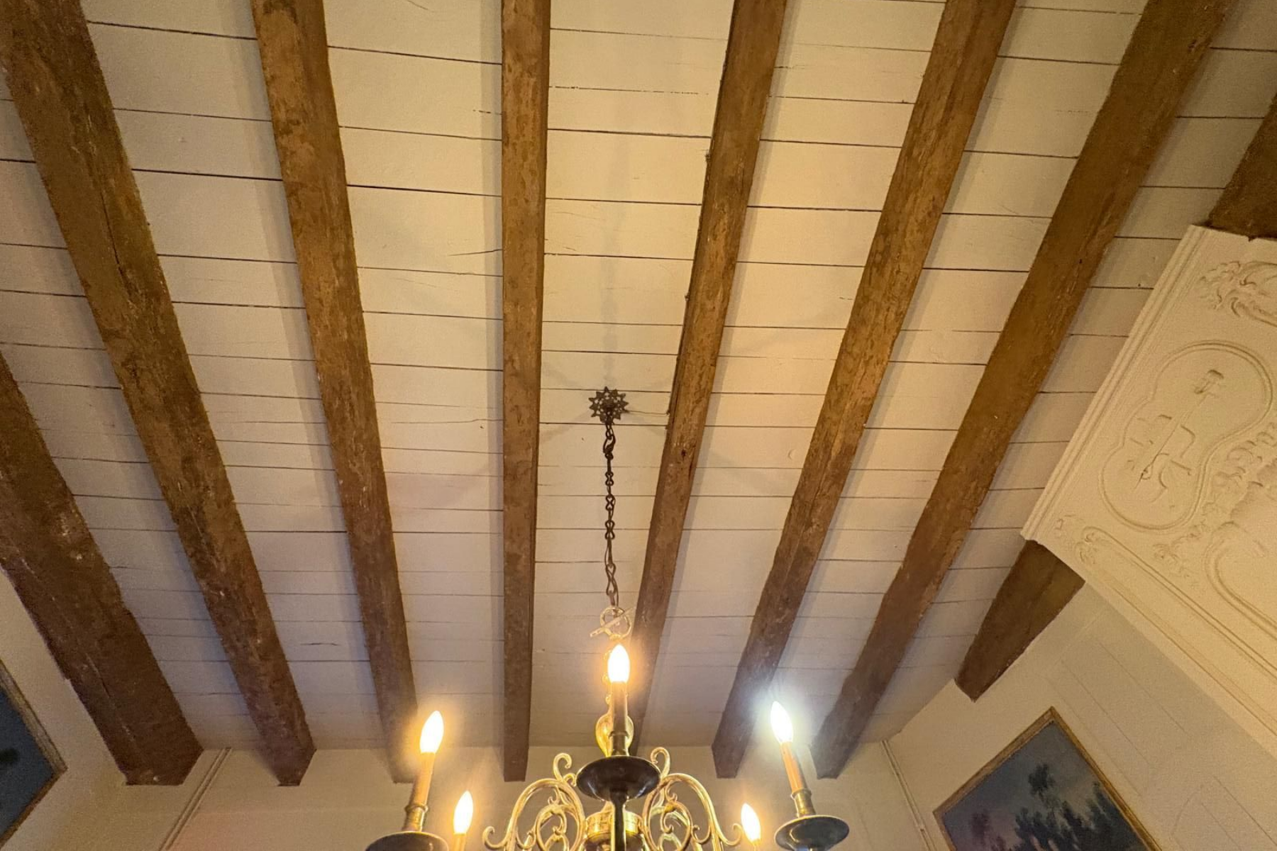 Des poutres en bois soutiennent un plafond blanc ; un lustre est suspendu en dessous.