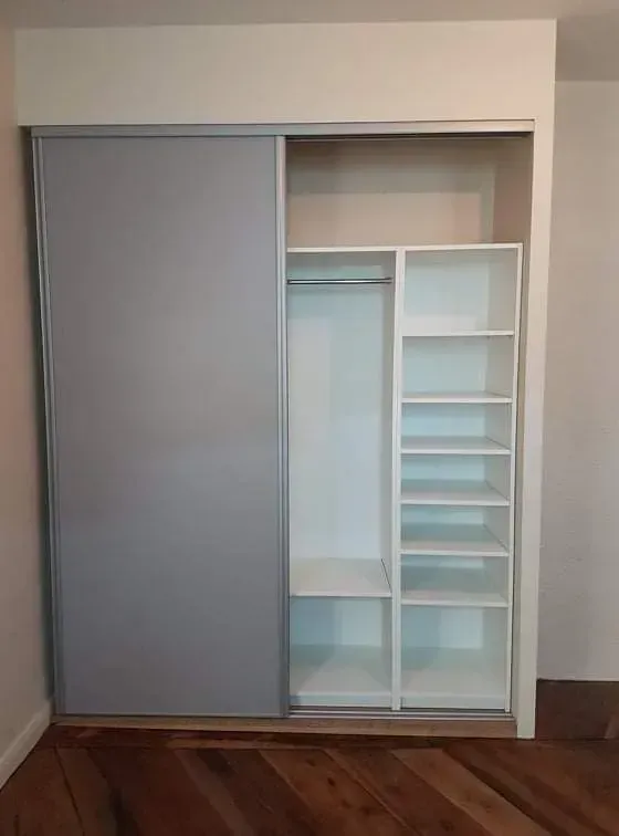 Placard blanc avec porte coulissante grise, étagères et tringle à vêtements contre un mur.