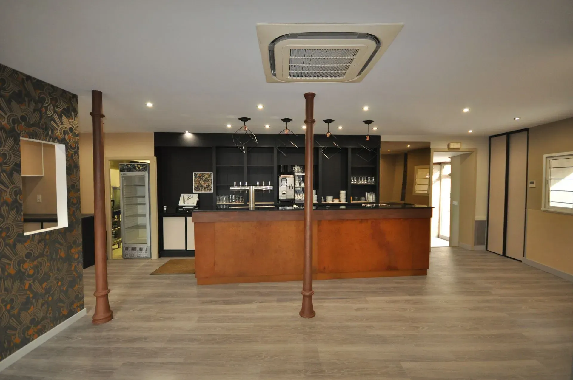 Intérieur de bar vide avec comptoir marron, étagères et sol gris.