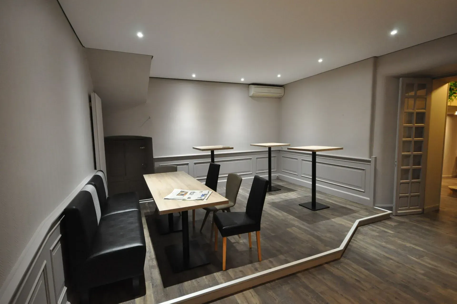 Intérieur d'un café vide avec tables, chaises et une banquette. Sol en bois et murs gris.