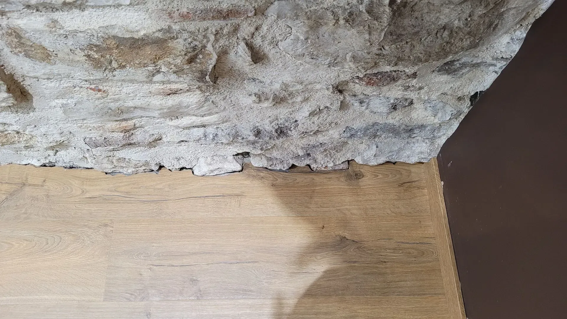 Un mur de pierre rencontre une poutre en bois ; couleurs brunes et beiges.