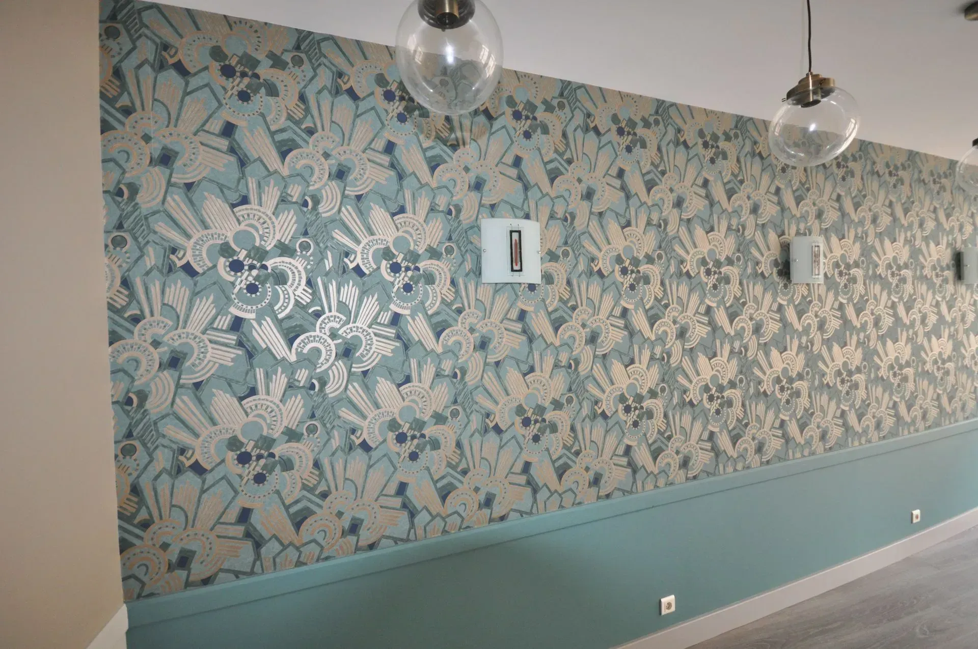 Mur recouvert de papier peint floral turquoise, de moulures turquoise et de suspensions lumineuses sphériques.