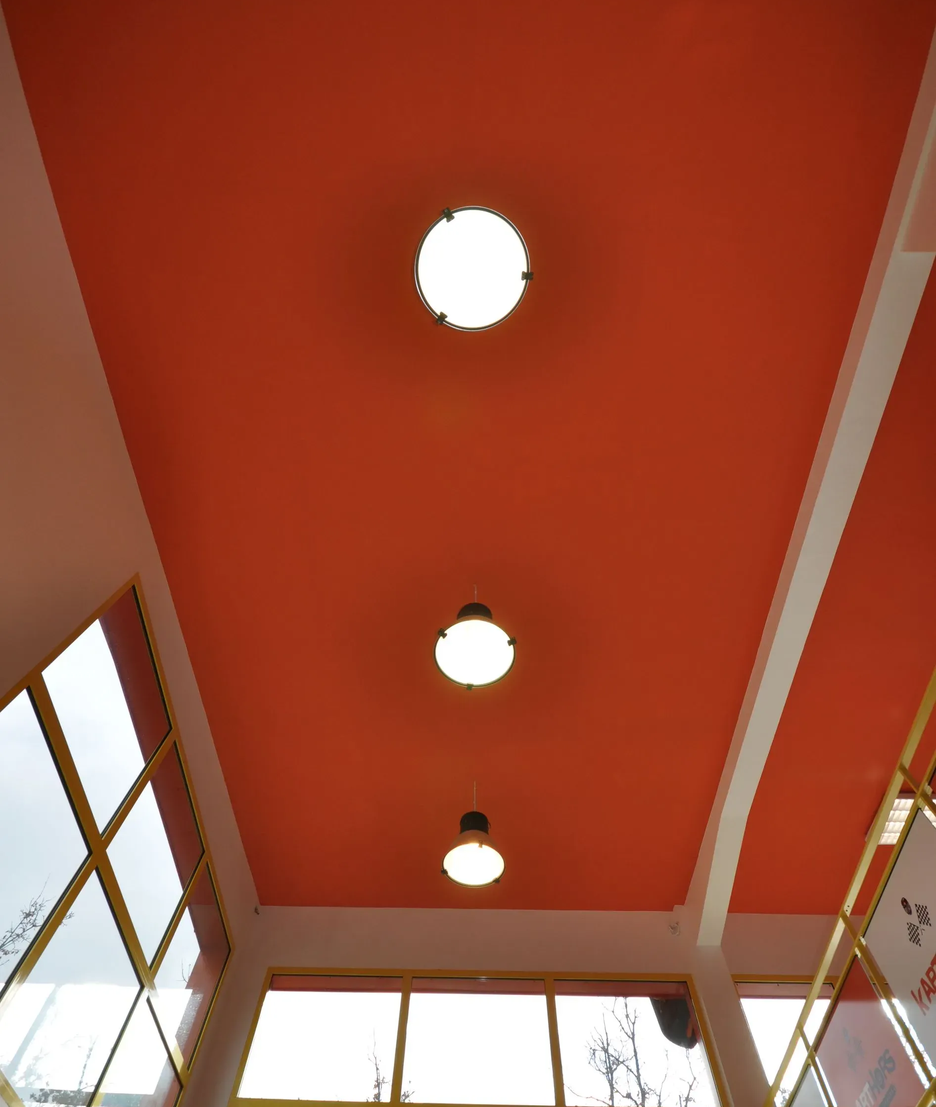 Plafond orange avec trois spots ronds. Morceau blanc autour du plafond. Fenêtres à encadrement jaune.