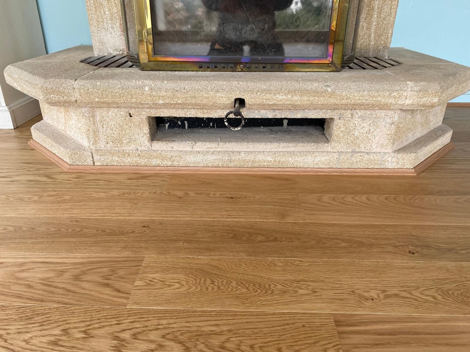 Cheminée en pierre beige sur parquet en bois brun clair.