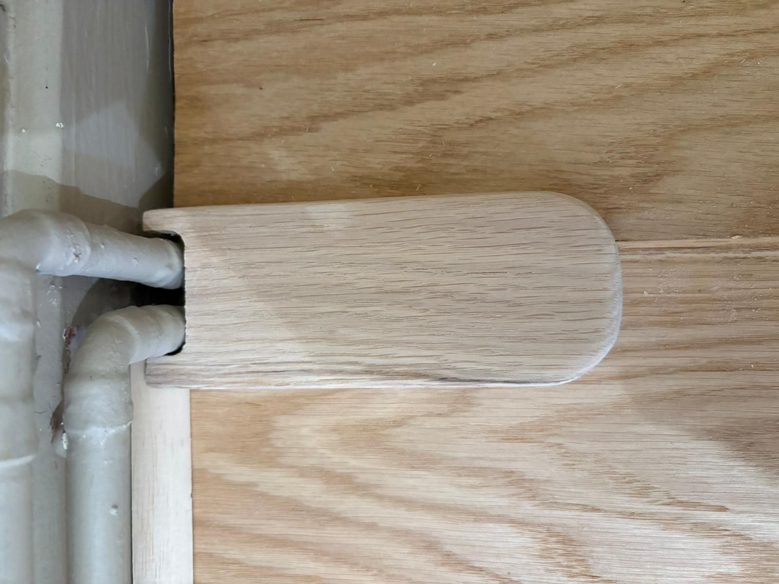 Cache en bois dissimulant deux tuyaux sortant du mur.