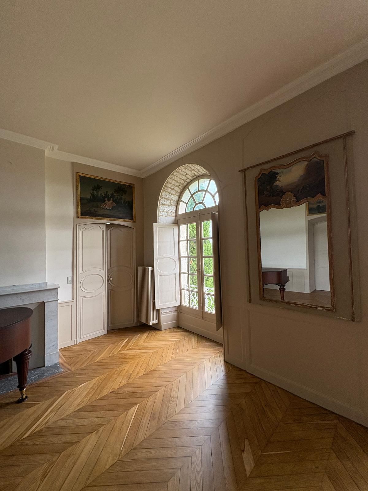 Les pieds d'une personne sur un parquet, près d'un mur blanc, avec des outils : meuleuse d'angle, marteau, pistolet à calfeutrer.