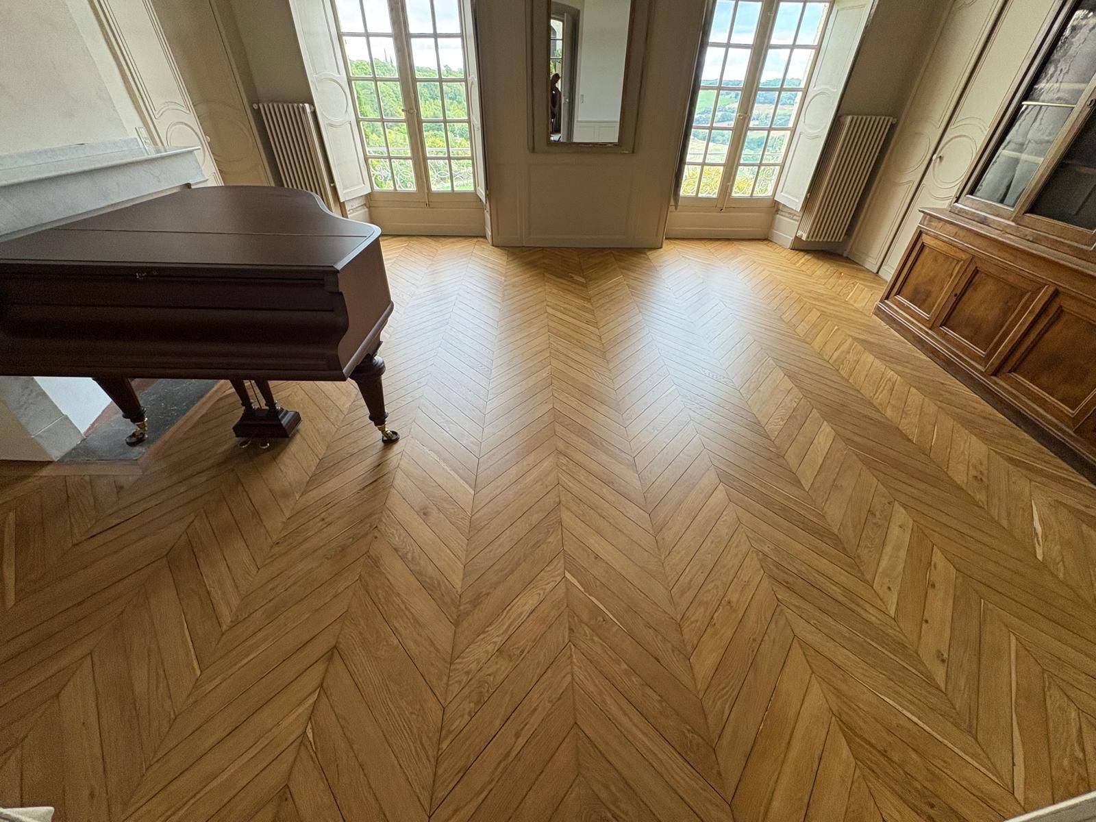 Parquet en bois, piano à queue et fenêtres.
