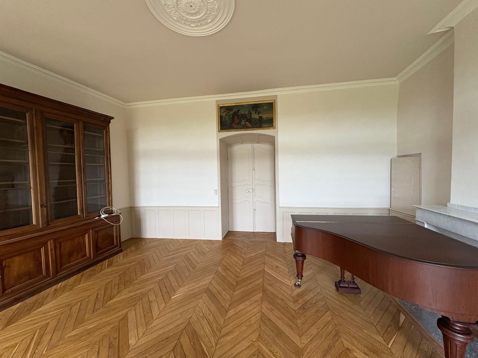 Pièce avec parquet, grande armoire en bois, piano à queue et porte.