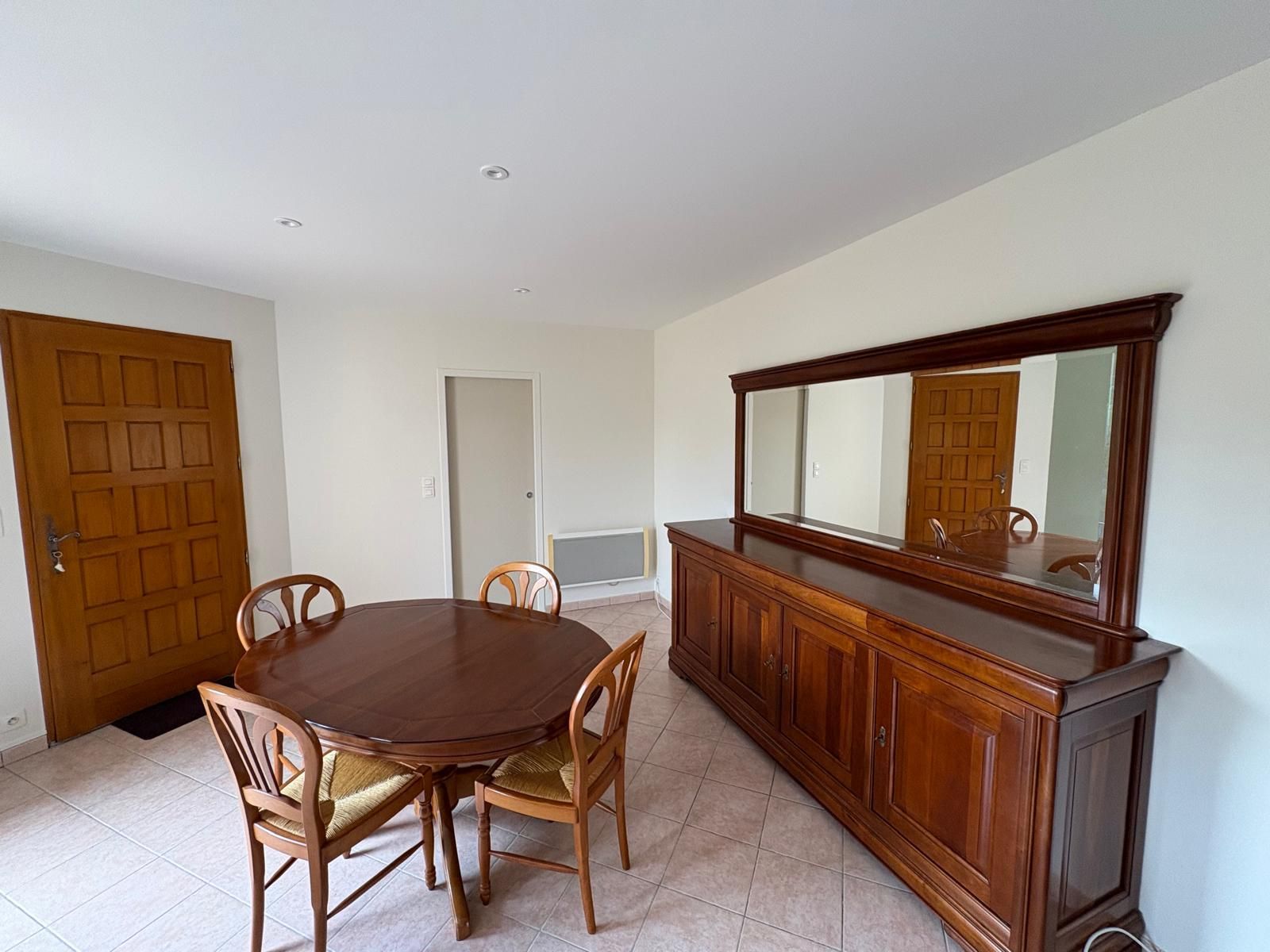 Salle à manger avec table en bois, chaises et buffet avec miroir. Portes en arrière-plan.