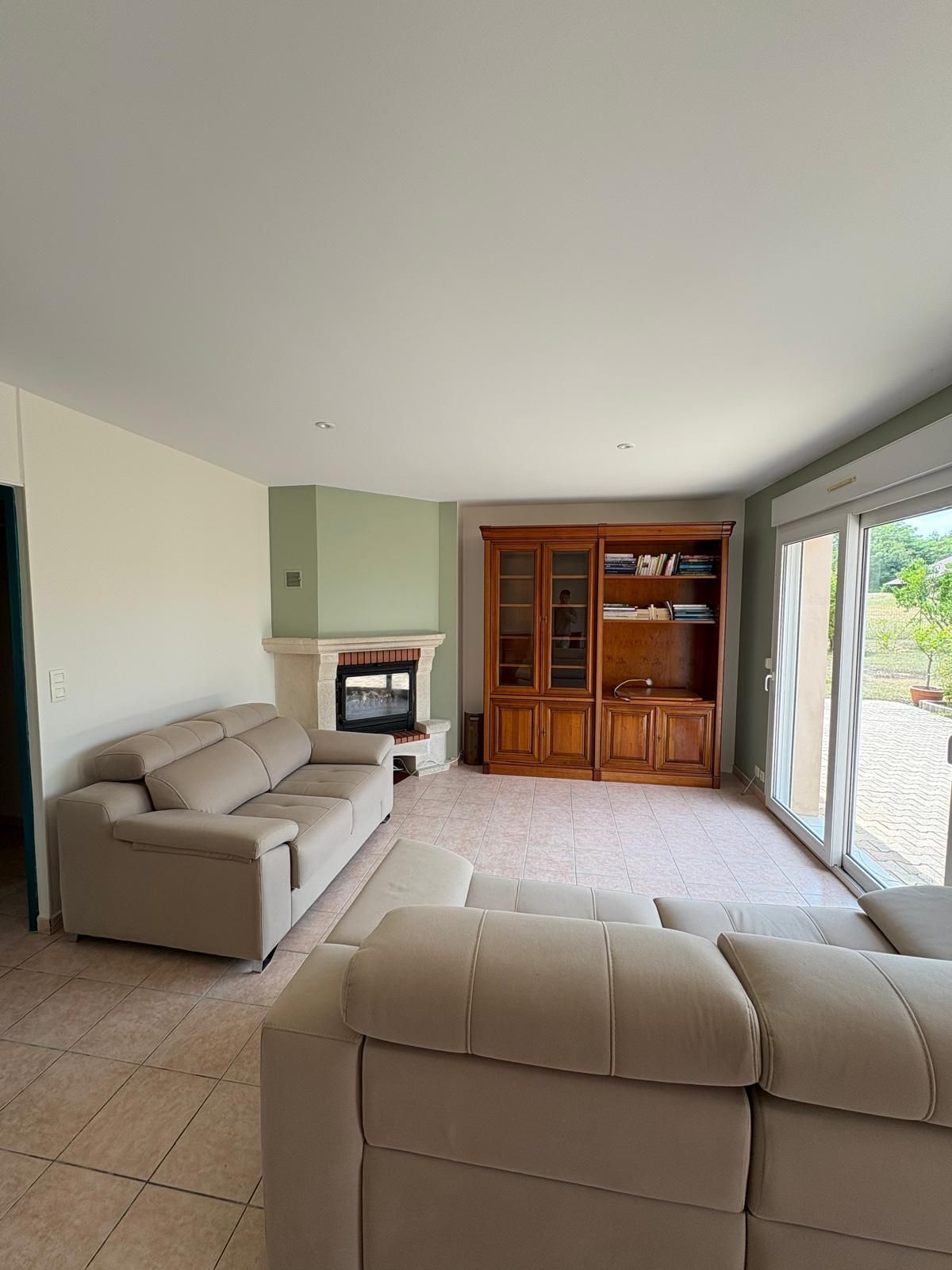 Salon avec canapés beiges, cheminée, armoire en bois et porte-fenêtre coulissante.