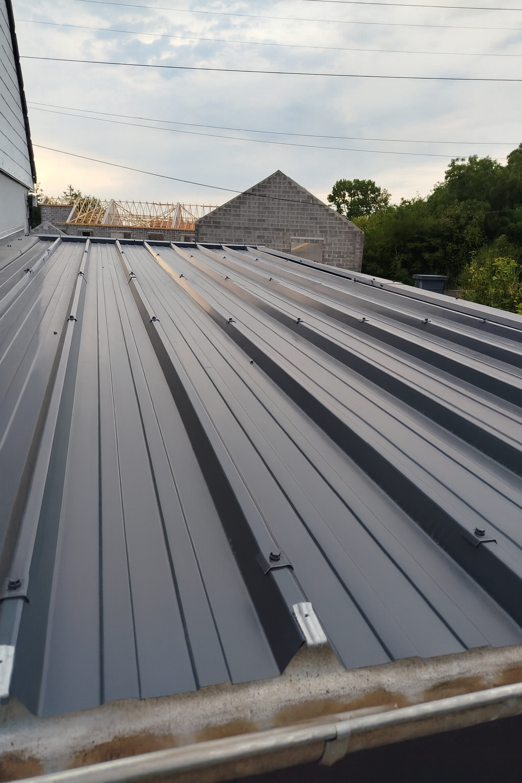 Toit en métal gris à nervures verticales, ciel nuageux.