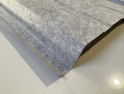 Gros plan sur une tôle de toiture ondulée recouverte d'un matériau gris feutré sur une surface grise.