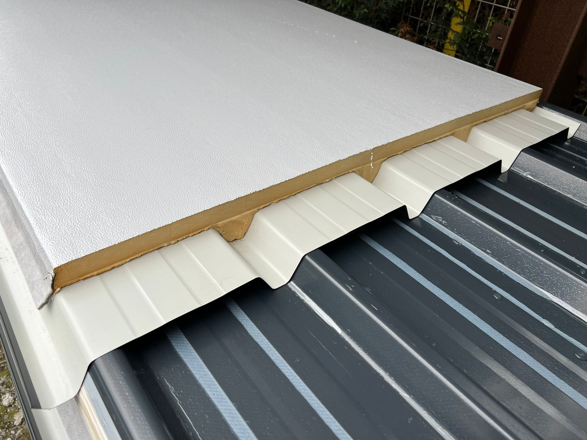 Installation de panneaux de toiture isolants : panneau en mousse blanche sur tôle ondulée avec supports beiges.