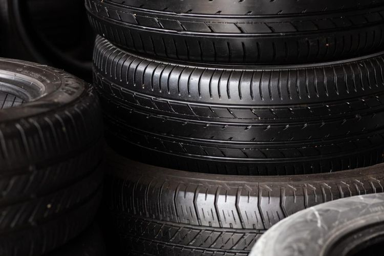 Apiladas llantas negras de coche en una tienda o garaje con poca luz.