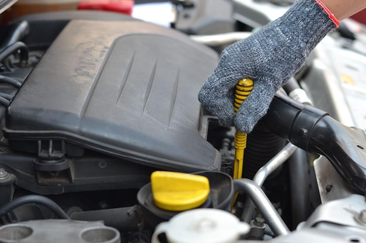 Una mano enguantada revisa la varilla medidora del aceite del motor en el compartimento del motor de un automóvil.