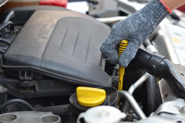 Una mano enguantada revisa la varilla medidora del aceite del motor en el compartimento del motor de un automóvil.