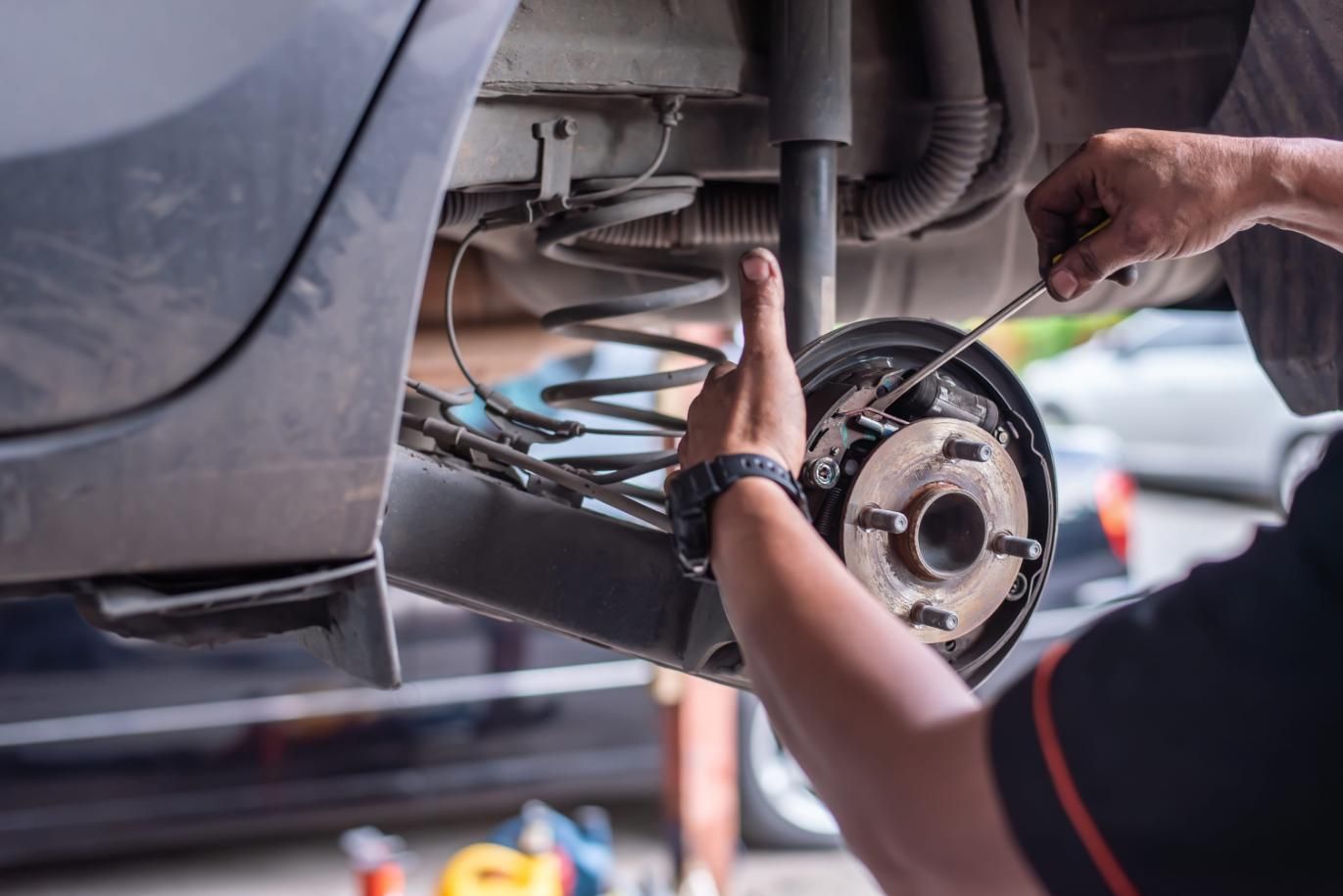 Mecánico trabajando debajo de un coche, apretando el conjunto del disco de freno con herramientas.