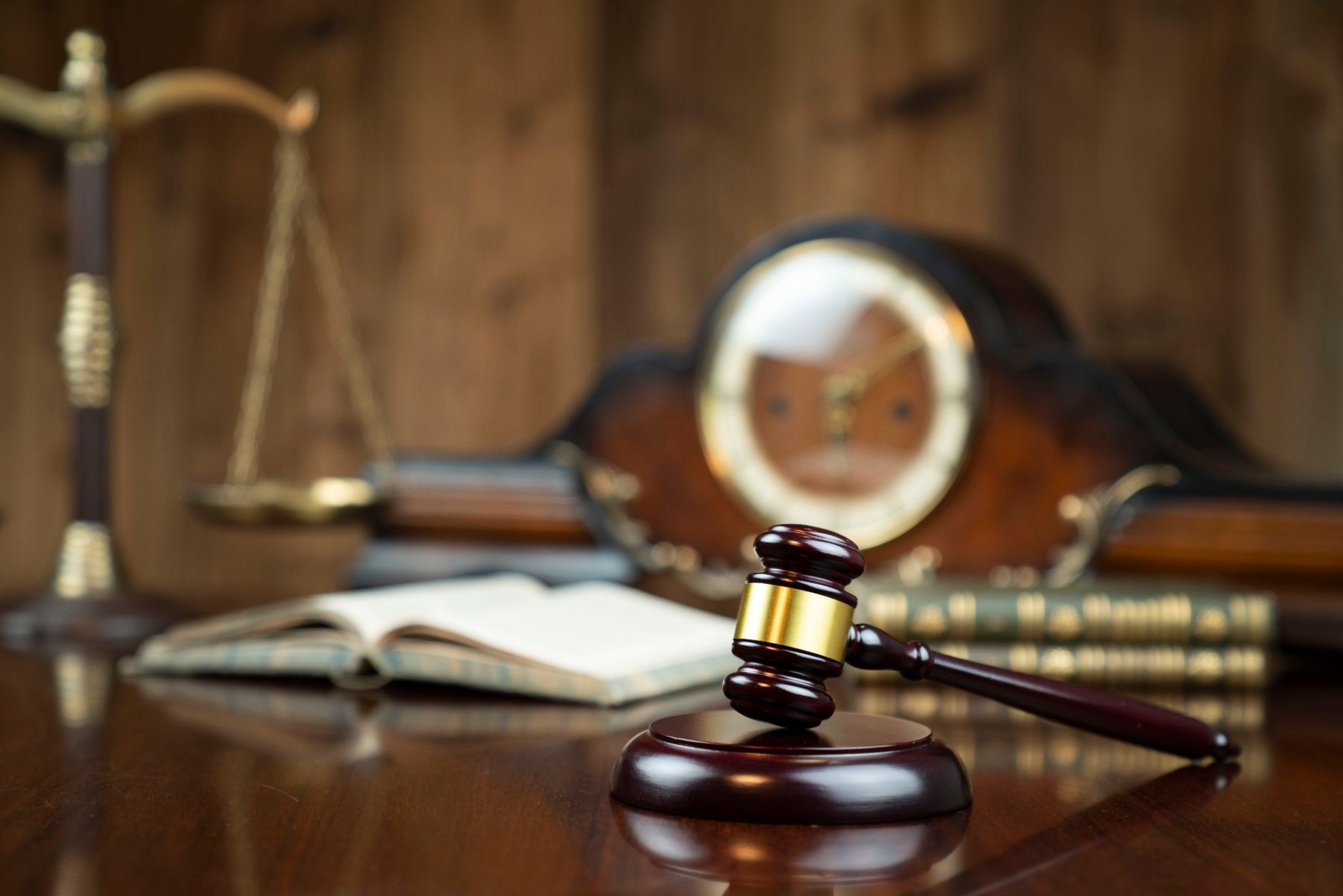 Un mazo y libros de leyes con una balanza y un reloj de arena en el fondo, lo que implica procedimientos legales.