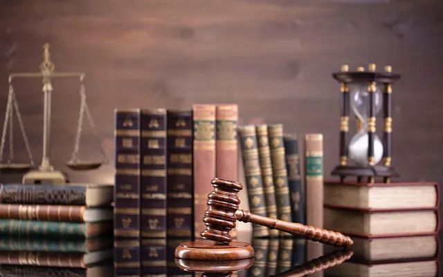 Un mazo y libros de leyes con una balanza y un reloj de arena en el fondo, lo que implica procedimientos legales.