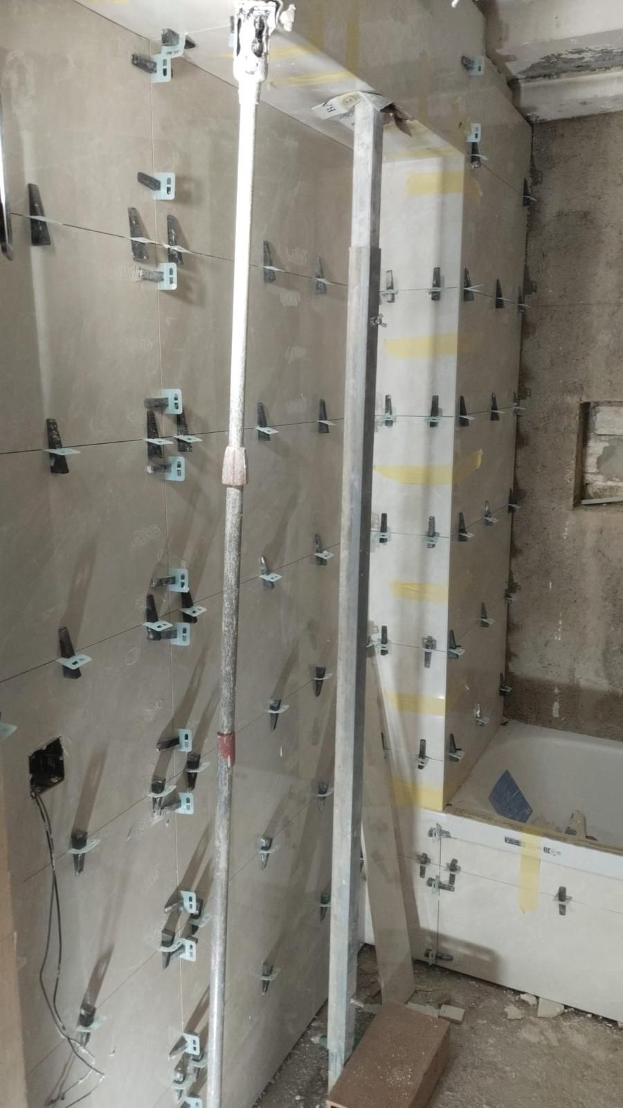 Baño con instalación de azulejos en proceso, paredes revestidas con clips de sistema de nivelación.