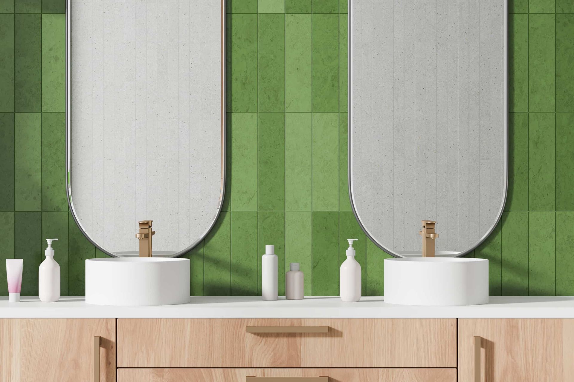 Dos lavabos con grifería dorada, bajo grandes espejos arqueados, contra una pared de azulejos verdes. Tocador de madera.