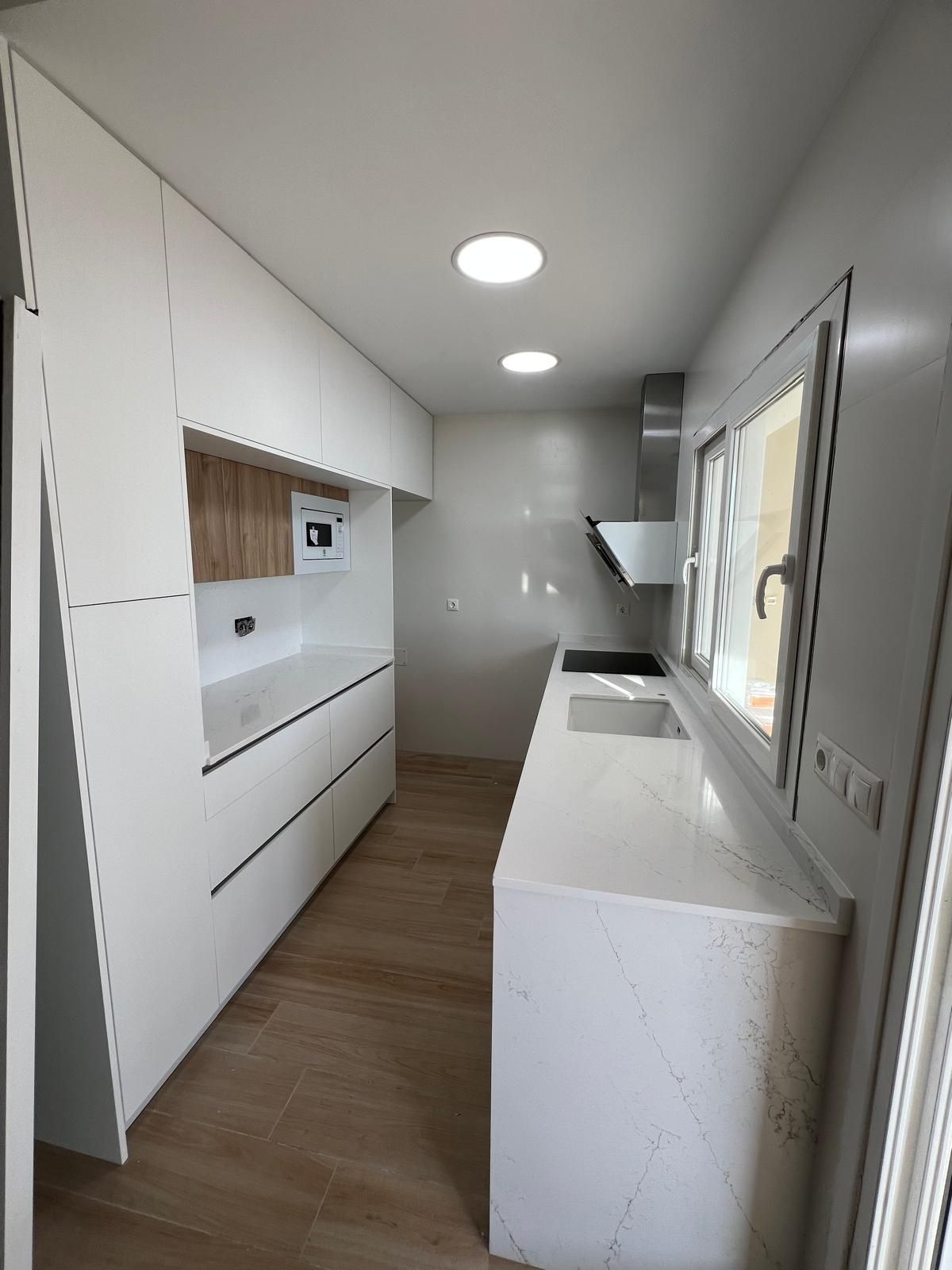 Cocina blanca moderna con encimeras de cuarzo, detalles en tonos madera y electrodomésticos de acero inoxidable.