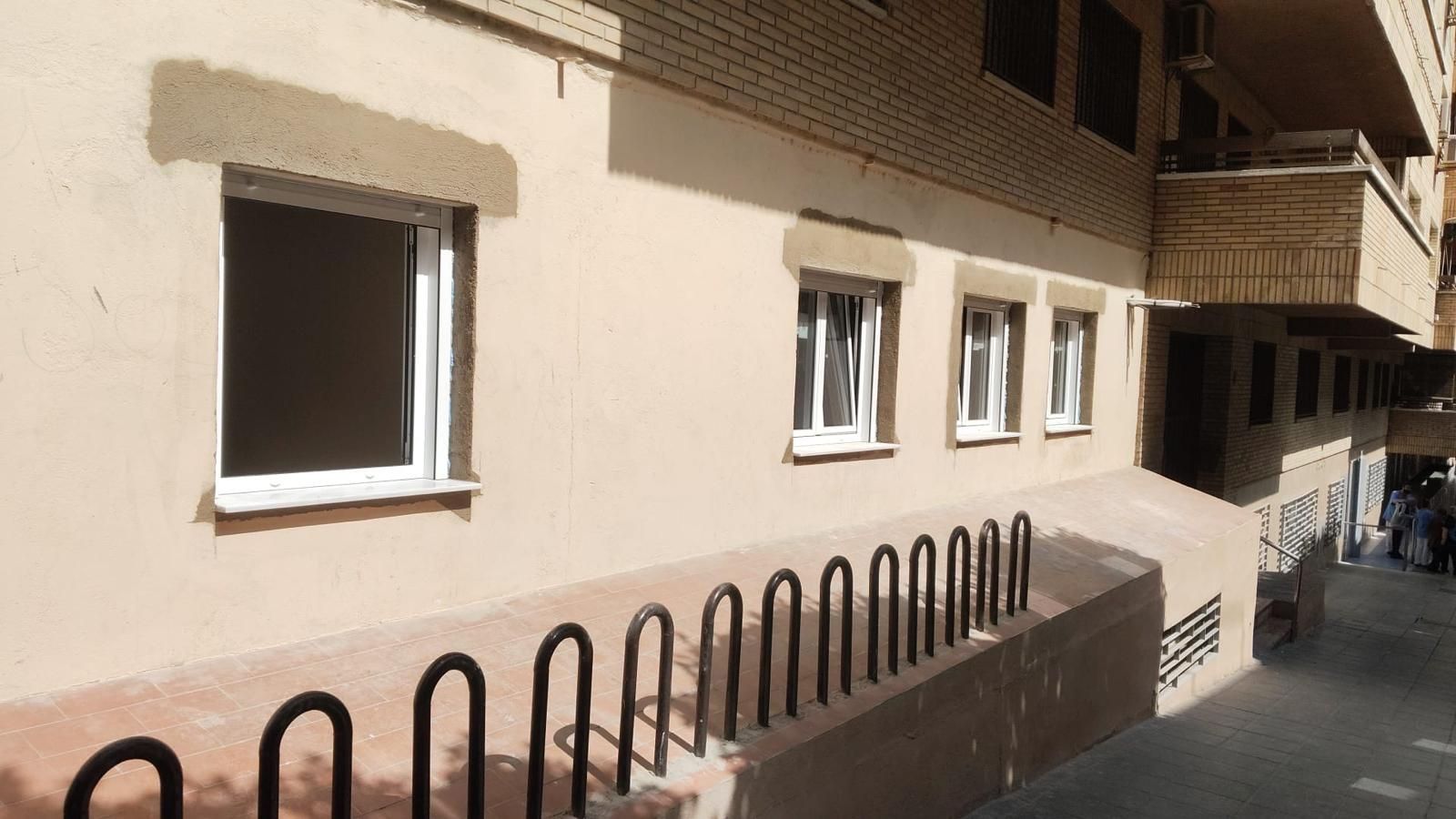 Exterior de un edificio con ventanas, aparcabicicletas y una paleta de colores tostado y marrón. Día soleado.