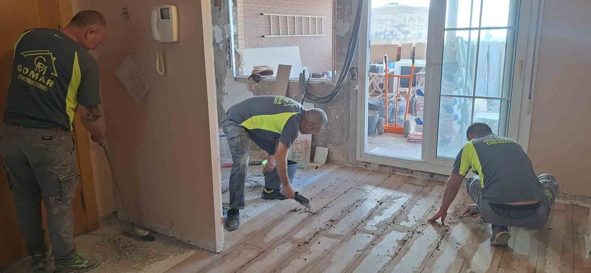Tres trabajadores reparando un suelo de madera.
