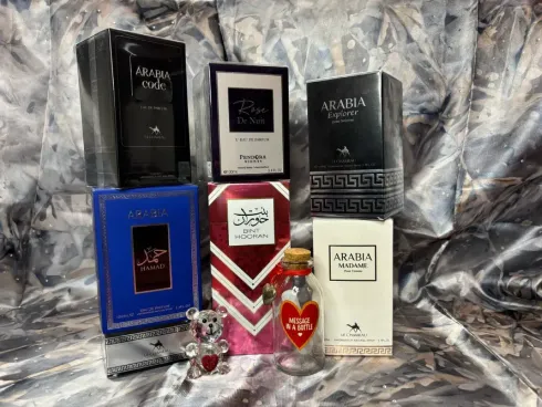 Colección de cajas de perfume y un tarro decorativo con forma de corazón, dispuestos sobre un fondo de tela arrugada.