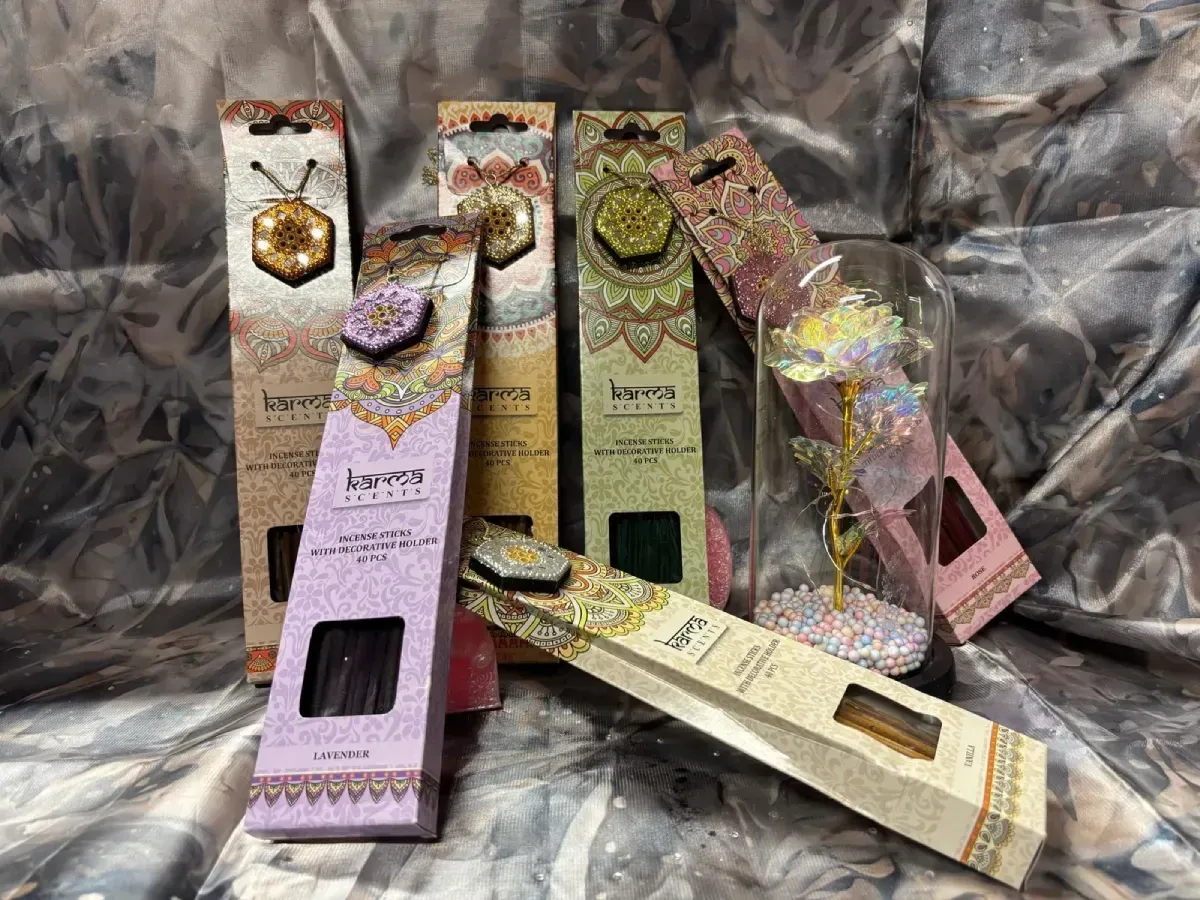 Varitas de incienso en cajas de colores y una rosa dentro de una cúpula de cristal sobre un fondo estampado.