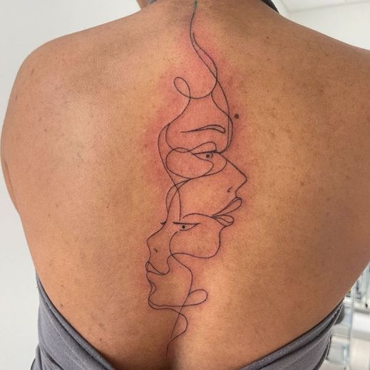 Une femme a un tatouage de deux visages dans le dos.