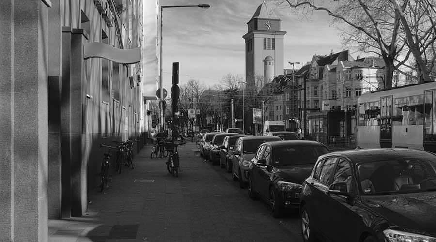 Ein Schwarzweißfoto einer Stadtstraße mit am Straßenrand geparkten Autos.