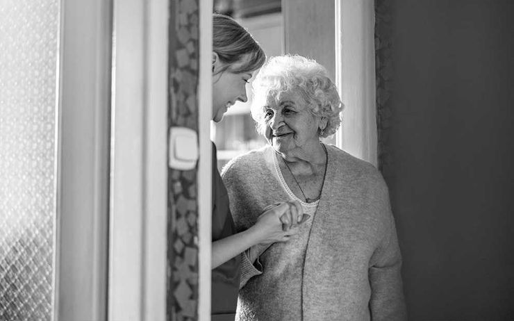 Pflegerin hält lächelnd Hand von Seniorin in Türrahmen Pflegerin hält lächelnd Hand von Seniorin in Türrahmen