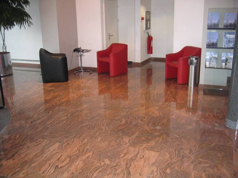 Eine Hotel- oder Bürolobby mit glänzendem Marmorboden, einem schwarzen Stuhl und zwei roten Stühlen.