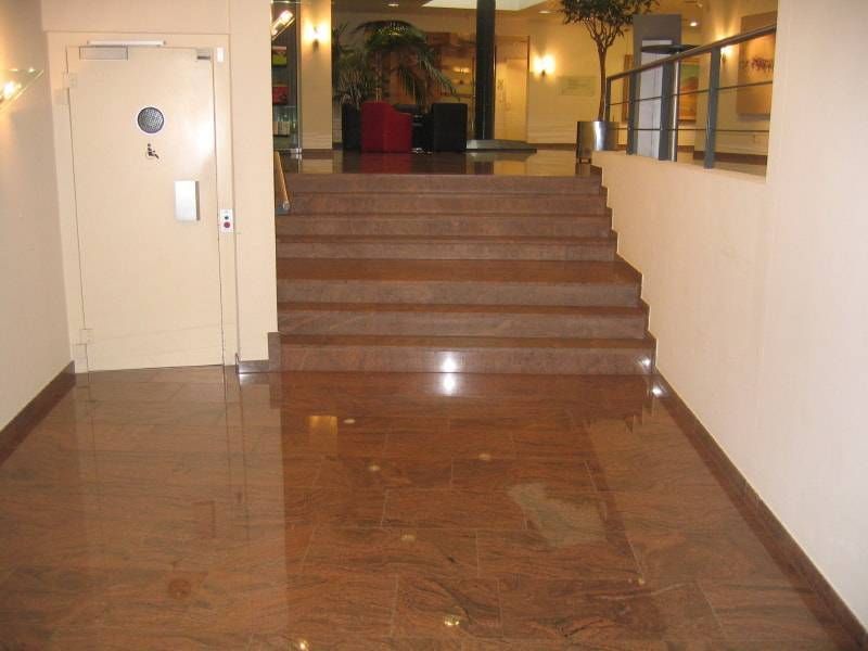 Eine Treppe aus braunem Marmor führt hinauf zu einem Vorraum mit einer geschlossenen Tür auf der linken Seite und einem Geländer auf der rechten Seite.