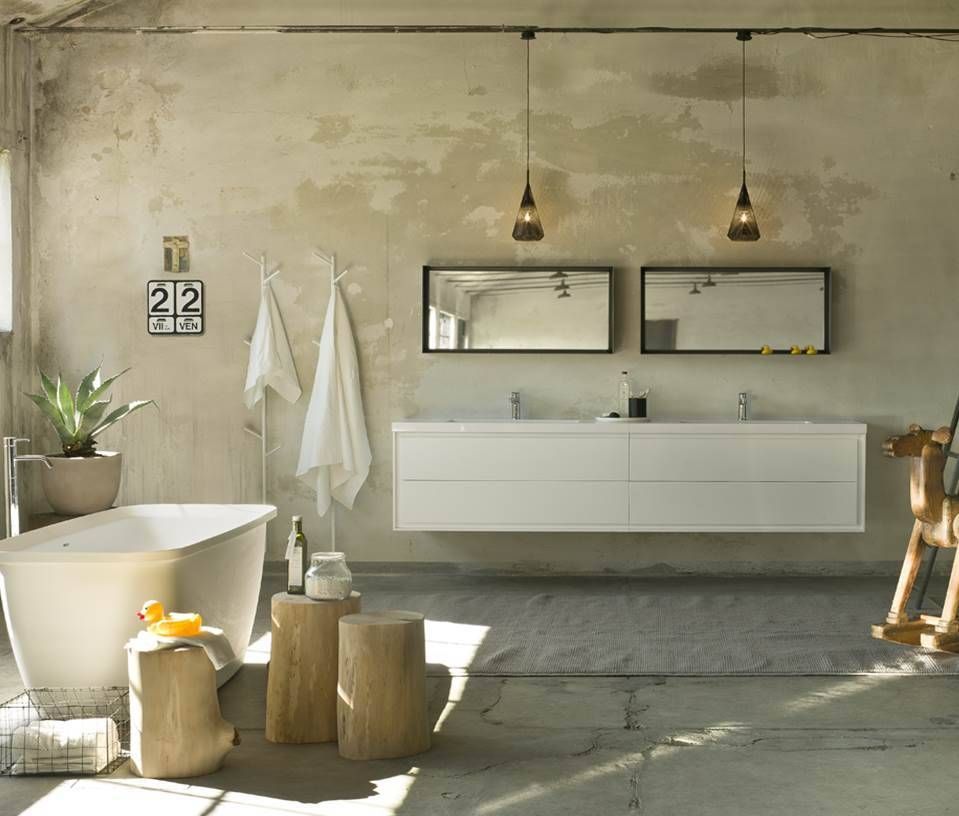 Ein modernes Badezimmer mit Doppelwaschbecken, Badewanne, zwei Pendelleuchten und rustikalen Betonwänden.